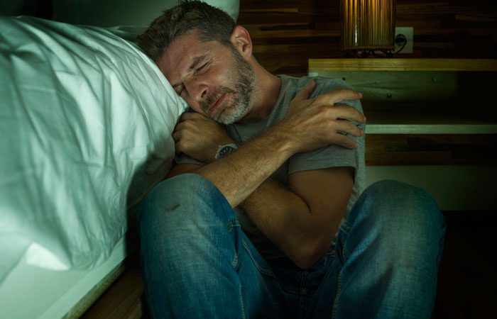 depressed man in pain sitting on floor beside bed