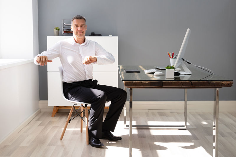 man sitting in office chair stretching to lessen back and sciatica nerve pain