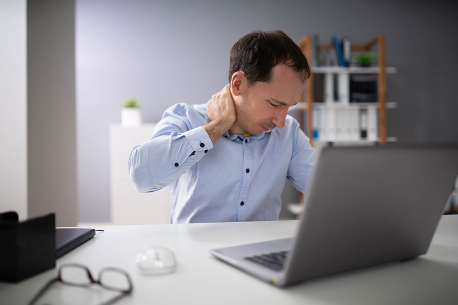 man with upper back neck pain sitting at laptop