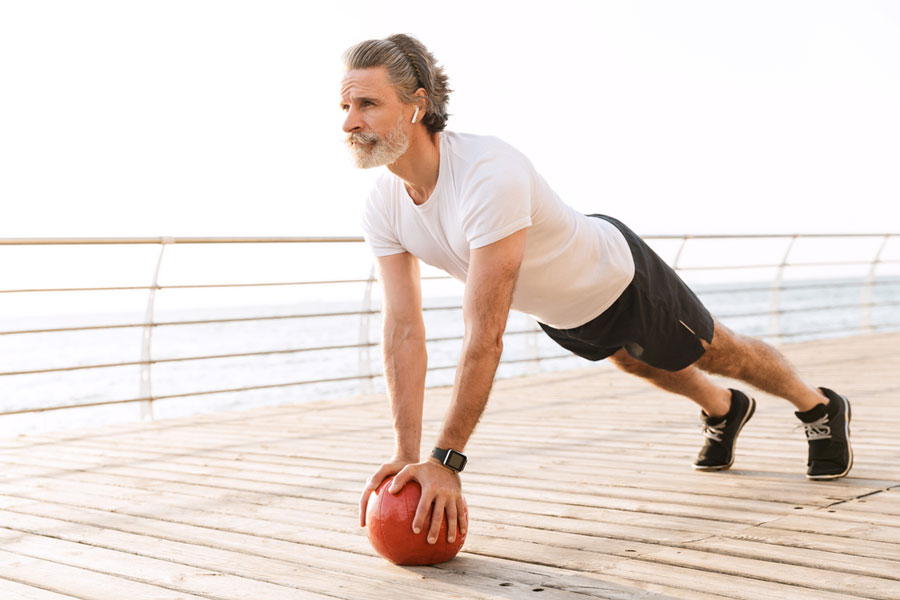 senior man on wooden deck performing front plank core exercise to prevent lower back pain