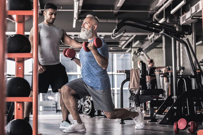 senior man with personal trainer doing exercise for lower back pain