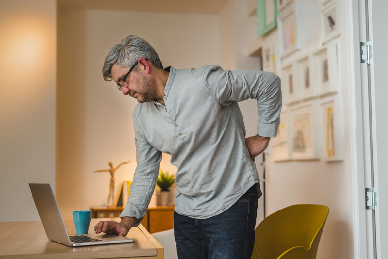 man looking at laptop with chronic lower back pain