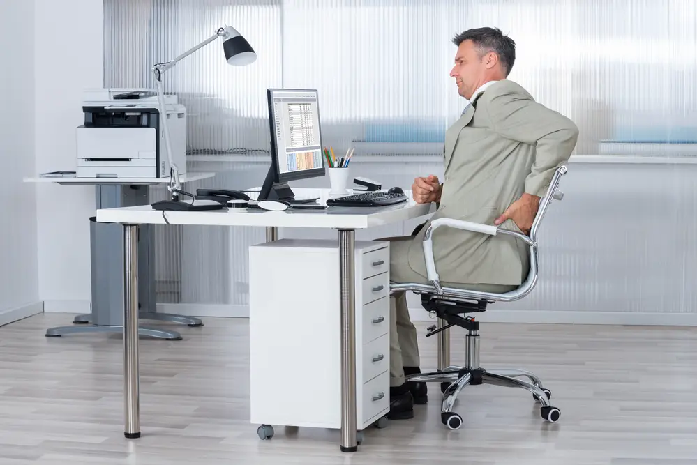 man at computer desk holding his lower back in pain