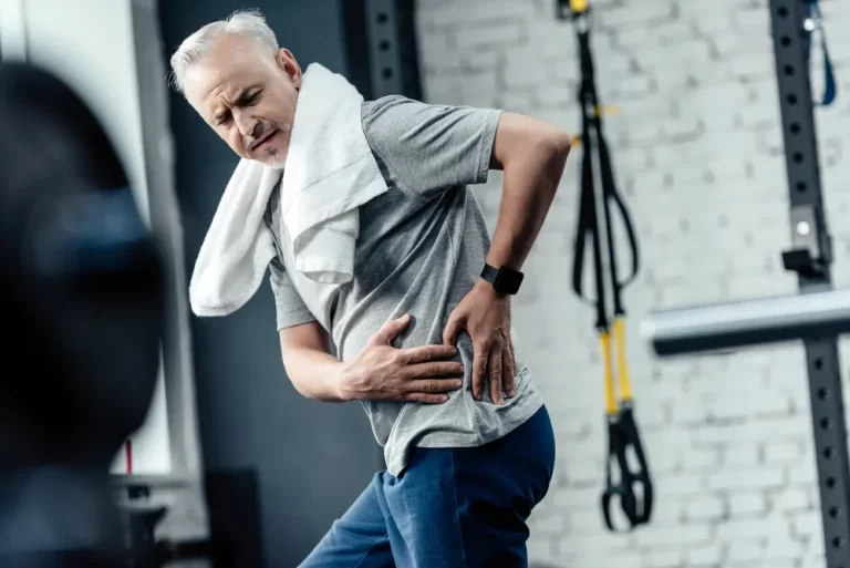 mature man in the gym holding his low back herniated disc