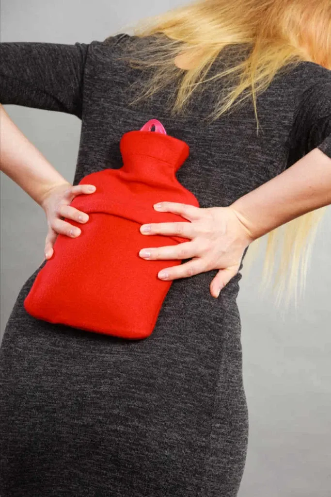 woman holding hot water bottle to her low back for pain relief