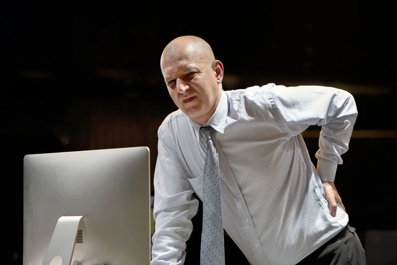 middle aged man in front of computer holding his low back pain