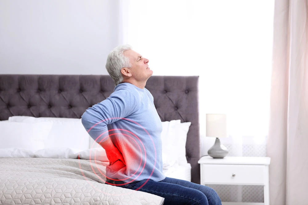 middle aged man sitting on bed with low back pain